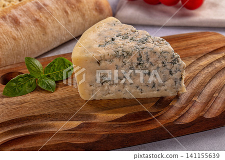 Wedged blue cheese on wooden board with basil and bread Wedged blue cheese on wooden board with basil and bread 141155639