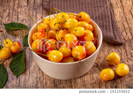 Bowl of fresh yellow cherries on rustic wooden table with green leaves 141155652