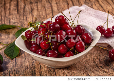 Fresh ripe cherries in white ceramic bowl on rustic wooden table Fresh ripe cherries in white ceramic bowl on rustic wooden table 141155653