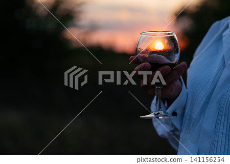 Woman with a glass of wine on vacation. Silhouette of the setting sun in the glass. Soft sunlight. Woman with a glass of wine on vacation. Silhouette of the setting sun in the glass. Soft sunlight. 141156254