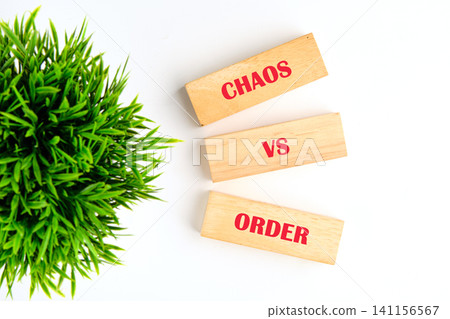 Wooden blocks display the words chaos and order with a small green plant beside them. This scene highlights the contrast between two concepts in a simple way Wooden blocks display the words chaos and order with a small green plant beside them. This scene highlights the contrast between two concepts in a simple way 141156567