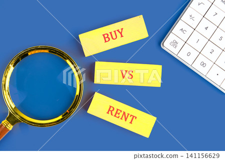 Three yellow cards with the words buy, vs, and rent are placed on a blue surface. A magnifying glass and a calculator are nearby, showing a comparison of housing choices Three yellow cards with the words buy, vs, and rent are placed on a blue surface. A magnifying glass and a calculator are nearby, showing a comparison of housing choices 141156629