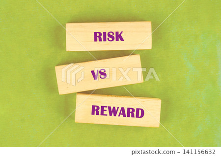 Three wooden blocks display the words risk, vs, and reward in a discussion about decision making. This scene is set on a flat surface during a workshop Three wooden blocks display the words risk, vs, and reward in a discussion about decision making. This scene is set on a flat surface during a workshop 141156632