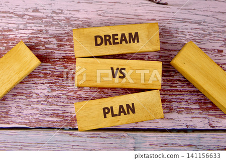 Wood blocks are arranged on a pink wooden surface with the words dream and plan. This shows a comparison between ideas and actions Wood blocks are arranged on a pink wooden surface with the words dream and plan. This shows a comparison between ideas and actions 141156633