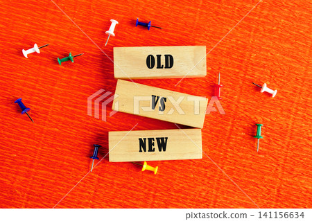 Wooden blocks display the words old and new with a vs in between. Colorful push pins are scattered on an orange surface, creating a vivid scene of contrast 141156634