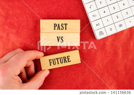 A person holds wooden blocks with the words past and future in a hand. A calculator is placed nearby on a red table. This shows a concept of time and choices A person holds wooden blocks with the words past and future in a hand. A calculator is placed nearby on a red table. This shows a concept of time and choices 141156636