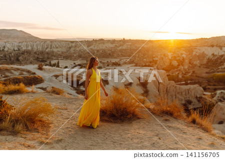 Young woman in yellow dress during sunrise watching hot air balloons in Cappadocia, Turkey Young woman in yellow dress during sunrise watching hot air balloons in Cappadocia, Turkey 141156705