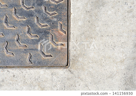 Cast iron manhole cover corner on a textured concrete surface Cast iron manhole cover corner on a textured concrete surface 141156930