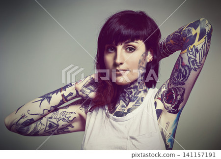 Portrait, tattoo or edgy woman in tank top on grey background for gothic style isolated in studio. Rockstar, unique or female punk model with ink on skin for body art, fashion or creative expression Portrait, tattoo or edgy woman in tank top on grey background for gothic style isolated in studio. Rockstar, unique or female punk model with ink on skin for body art, fashion or creative expression 141157191