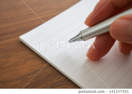 Close-up of a woman's fingertips holding a notebook and ballpoint pen. Close-up of a woman's fingertips holding a notebook and ballpoint pen. 141157301