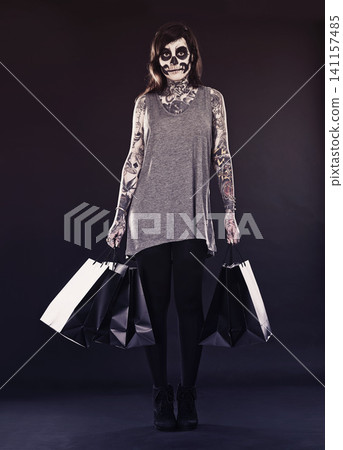 Woman, skull makeup and shopping bags in studio on dark background with retail and discount for halloween. Portrait, female person and tattoo with edgy or creative style, body art and confidence Woman, skull makeup and shopping bags in studio on dark background with retail and discount for halloween. Portrait, female person and tattoo with edgy or creative style, body art and confidence 141157485