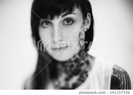 Portrait, tattoo and gothic woman in a tank top on black and white background for edgy style in studio. Face, unique and female punk model with ink on skin for art, fashion or creative expression Portrait, tattoo and gothic woman in a tank top on black and white background for edgy style in studio. Face, unique and female punk model with ink on skin for art, fashion or creative expression 141157536
