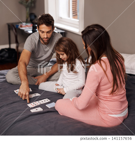 Parents, girl and playing cards to relax for fun with bonding, learning and games with strategy in home bedroom. Father, mother and daughter on bed, maths and teaching with connection in family house Parents, girl and playing cards to relax for fun with bonding, learning and games with strategy in home bedroom. Father, mother and daughter on bed, maths and teaching with connection in family house 141157656