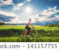Female cyclist riding mountain bike through vibrant green meadow 141157755