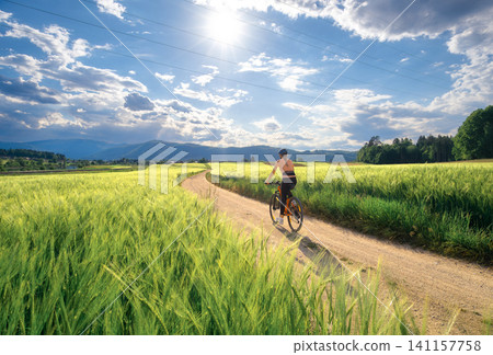 Woman riding mountain bike on dirt road and green wheat fields Woman riding mountain bike on dirt road and green wheat fields 141157758