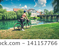 Female cyclist with gravel bike standing on green grass and rive 141157766