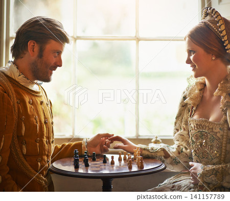 Renaissance, couple and chess at home with holding hands, vintage and medieval costume in a palace. Window, luxury and queen together with smile from strategy game and talking while playing with love Renaissance, couple and chess at home with holding hands, vintage and medieval costume in a palace. Window, luxury and queen together with smile from strategy game and talking while playing with love 141157789