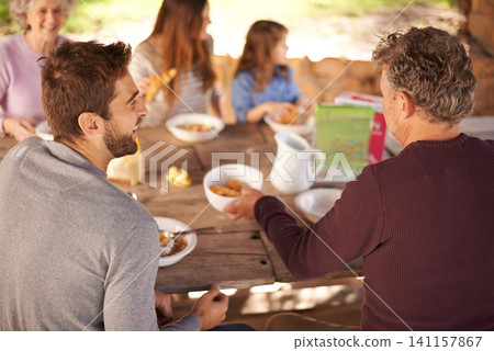 Outdoor, women and men with family for picnic in nature of backyard of house, smile and joy. Group of people and child eating breakfast on table of wood in summer, happiness and love together in home Outdoor, women and men with family for picnic in nature of backyard of house, smile and joy. Group of people and child eating breakfast on table of wood in summer, happiness and love together in home 141157867