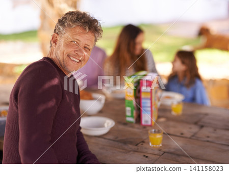 Portrait, mature and man with smile for picnic with family in nature of backyard of house and outdoor. Women, men and child eating breakfast on table of wood in summer, happiness and love in home Portrait, mature and man with smile for picnic with family in nature of backyard of house and outdoor. Women, men and child eating breakfast on table of wood in summer, happiness and love in home 141158023