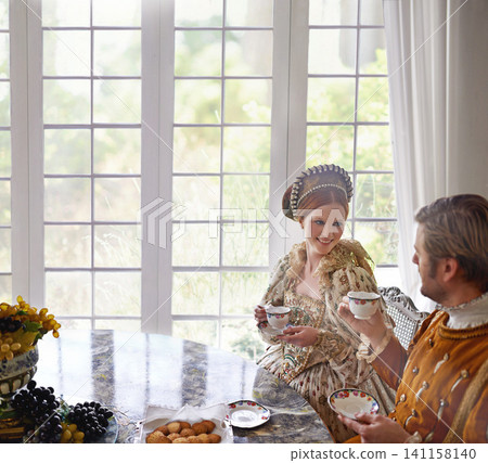 King, queen and couple with tea in costume, smile and conversation in vintage clothes in castle at breakfast. Woman, man and drink together in morning with Victorian fashion at regal palace in UK 141158140