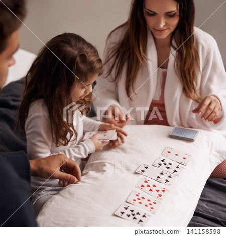 Mom, father and girl with playing cards for game with bonding, learning and relax with strategy in bedroom. Dad, mother and daughter with deal, deck and child on bed with connection in family house 141158598