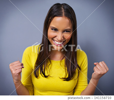 Woman, fist and celebration with smile in studio for success, goals and vision for achievement by blue background. Girl, person and winner with cheers, thinking and excited with competition in Mexico Woman, fist and celebration with smile in studio for success, goals and vision for achievement by blue background. Girl, person and winner with cheers, thinking and excited with competition in Mexico 141158710