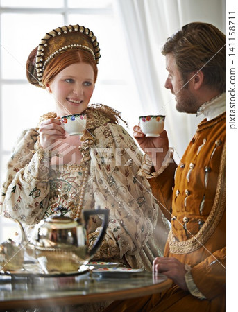 King, queen and couple with tea for royalty, smile and conversation in vintage clothes with style in castle. Woman, man and drink together in morning with Victorian fashion at regal palace in UK King, queen and couple with tea for royalty, smile and conversation in vintage clothes with style in castle. Woman, man and drink together in morning with Victorian fashion at regal palace in UK 141158711