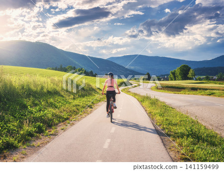 Woman riding mountain bike on asphalt bicycle path in countrysid Woman riding mountain bike on asphalt bicycle path in countrysid 141159499