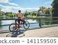 Female cyclist with mountain bike standing on wooden bridge 141159505