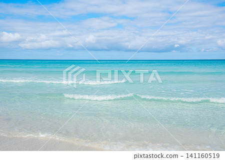 Calm ocean waves gently lap on the sandy shore under a bright blue sky Calm ocean waves gently lap on the sandy shore under a bright blue sky 141160519