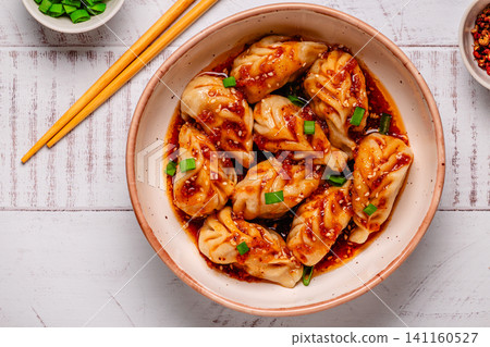 Delicious dumplings served in a bowl with a spicy sauce and green onions Delicious dumplings served in a bowl with a spicy sauce and green onions 141160527