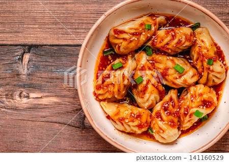Delicious dumplings served in a bowl with a spicy sauce and green onions Delicious dumplings served in a bowl with a spicy sauce and green onions 141160529