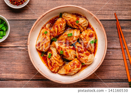 Delicious dumplings served in a bowl with a spicy sauce and green onions Delicious dumplings served in a bowl with a spicy sauce and green onions 141160530