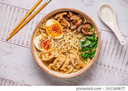 Bowl of noodles with dumplings, egg, and mushrooms on a wooden table Bowl of noodles with dumplings, egg, and mushrooms on a wooden table 141160677