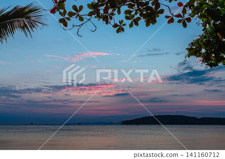Sunset over calm beach with fishing boats and silhouetted trees in the evening sky Sunset over calm beach with fishing boats and silhouetted trees in the evening sky 141160712