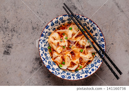 Wontons are placed in a bowl with spicy sauce. 141160736