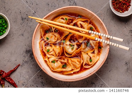 Wontons are placed in a bowl with spicy sauce. 141160746