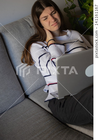 Young woman experiencing neck pain and displeasure while working remotely from home, feeling stressed and tired with deadlines, needing comfort and relief from discomfort Young woman experiencing neck pain and displeasure while working remotely from home, feeling stressed and tired with deadlines, needing comfort and relief from discomfort 141161167