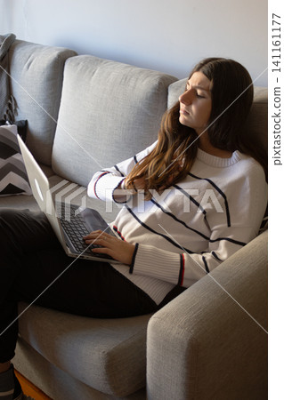Stressed young woman working from home on her laptop, sitting on a gray sofa with a tired and frustrated expression, dealing with a difficult job Stressed young woman working from home on her laptop, sitting on a gray sofa with a tired and frustrated expression, dealing with a difficult job 141161177