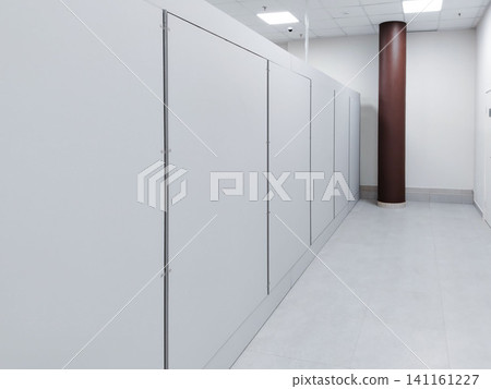 Modern interior of a commercial building featuring white storage cabinets along a corridor with a brown support column and gray tiled flooring 141161227
