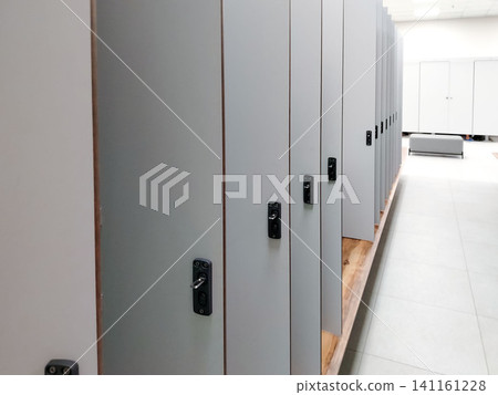 Row of gray lockers with black handles and locks in a modern changing room, clean tiled floor and bright lighting creating a spacious atmosphere Row of gray lockers with black handles and locks in a modern changing room, clean tiled floor and bright lighting creating a spacious atmosphere 141161228