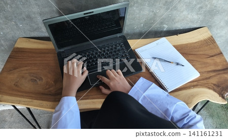 Muslim High School Student Typing on Laptop with Notebook on Wooden Table Muslim High School Student Typing on Laptop with Notebook on Wooden Table 141161231