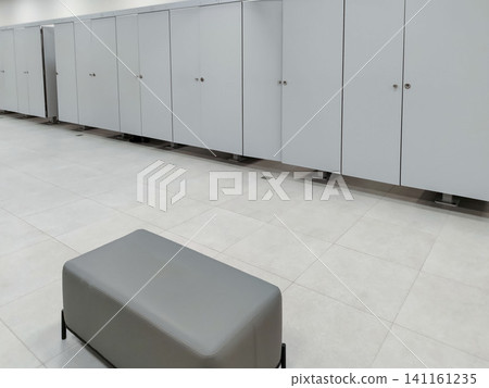 Modern changing room interior featuring gray lockers and a padded bench on tiled floor, designed for convenience and privacy in public facilities Modern changing room interior featuring gray lockers and a padded bench on tiled floor, designed for convenience and privacy in public facilities 141161235