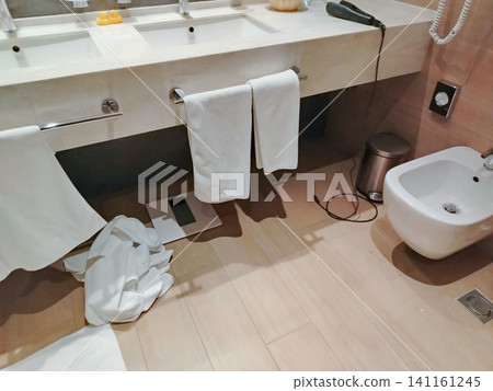 Modern bathroom interior featuring white towels hanging on a sink, a bidet, and a waste bin on a wooden floor with a clean, minimalist design Modern bathroom interior featuring white towels hanging on a sink, a bidet, and a waste bin on a wooden floor with a clean, minimalist design 141161245