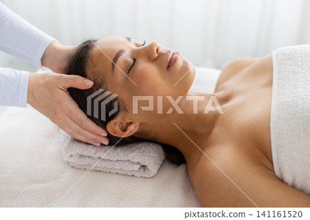 Therapist massaging young black womans scalp and temple area in spa Therapist massaging young black womans scalp and temple area in spa 141161520