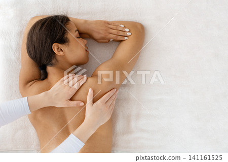 Young Black woman receiving gentle shoulder and back massage on spa bed Young Black woman receiving gentle shoulder and back massage on spa bed 141161525