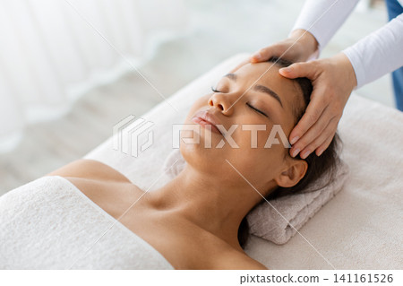 Young black woman getting head massage treatment at luxury spa Young black woman getting head massage treatment at luxury spa 141161526