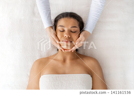 Top view of beautiful black woman enjoying facial spa treatment massage Top view of beautiful black woman enjoying facial spa treatment massage 141161536