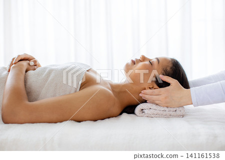 Young black woman relaxing on spa table while therapist massaging her head Young black woman relaxing on spa table while therapist massaging her head 141161538