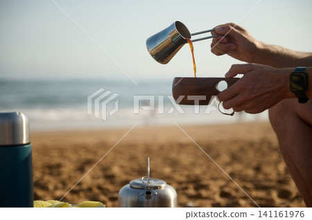Pouring coffee into a wooden cup on the beach during a relaxed camping morning Pouring coffee into a wooden cup on the beach during a relaxed camping morning 141161976